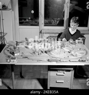 Junge in den 1950s. Ein Junge an seiner Modelleisenbahn, montiert auf einem Tisch in seinem Zimmer. Er leitet die Züge, wie schnell es geht und ob er will, dass der Zug vorwärts oder rückwärts fährt. Die Modelleisenbahn hat Häuser, Bäume, Tiere und Menschen in ihr als maßstabsgetrete Modelle. Höchstwahrscheinlich ein Zugsatz des deutschen Herstellers Fleischmann, da die Schienen das typische zweigleisige Gleichstrom-System sind. Schweden 1958. Conard Ref. 3867 Stockfoto