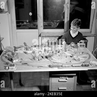 Junge in den 1950s. Ein Junge an seiner Modelleisenbahn, montiert auf einem Tisch in seinem Zimmer. Er leitet die Züge, wie schnell es geht und ob er will, dass der Zug vorwärts oder rückwärts fährt. Die Modelleisenbahn hat Häuser, Bäume, Tiere und Menschen in ihr als maßstabsgetrete Modelle. Höchstwahrscheinlich ein Zugsatz des deutschen Herstellers Fleischmann, da die Schienen das typische zweigleisige Gleichstrom-System sind. Schweden 1958. Conard Ref. 3867 Stockfoto