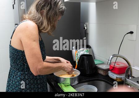 Junge Frau bereitet Käsekuchen in der Küche mit verschiedenen Zutaten zu. Familiengastronomie. Salvador, Bahia, Brasilien Stockfoto
