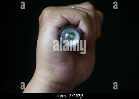 Eine LED-Taschenlampe, die in der Hand einer Person auf einem schwarzen Hintergrund gehalten wird. Nahaufnahme. Stockfoto