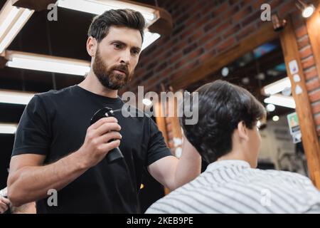 Friseur sprühen Wasser auf die Haare von verschwommenen Teenager Jungen im Schönheitssalon, Stockbild Stockfoto