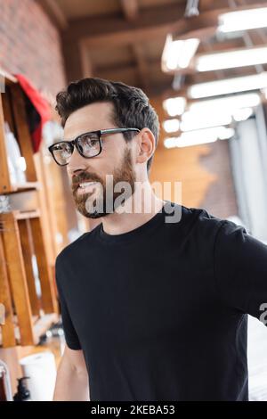 Bärtiger Barbier in Brillen und schwarzes T-Shirt im Barbershop, Stockbild Stockfoto