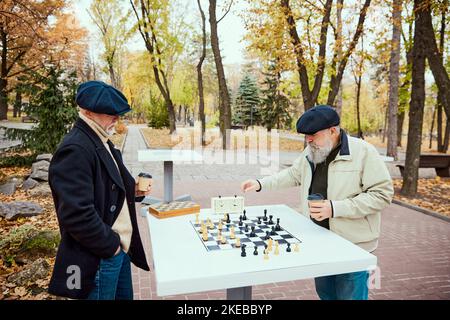 Porträt von zwei älteren Männern, die im Park an einem Herbsttagaus Schach spielen. Freizeit Hobby. Konzept der Freizeitgestaltung, alte Generation Stockfoto