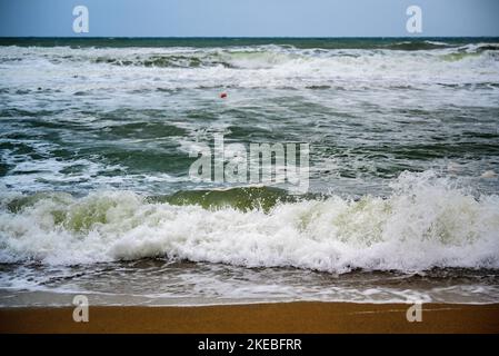 Stürmisches Meer, große Brandung und Welle bei windigem Wetter am Sandstrand, kleine Boje im Wasser, Morgen. Stockfoto