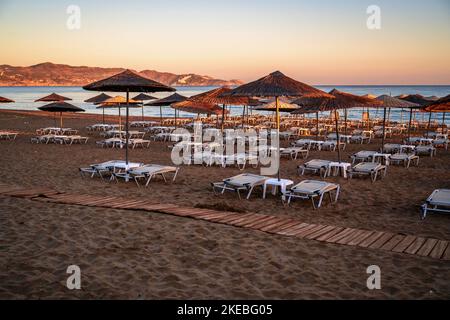 Leerer Strand mit Sonnenschirm und Liegestuhl in schöner Sonnenaufgangsbeleuchtung. Amoudara, Kreta, Strand. Stockfoto