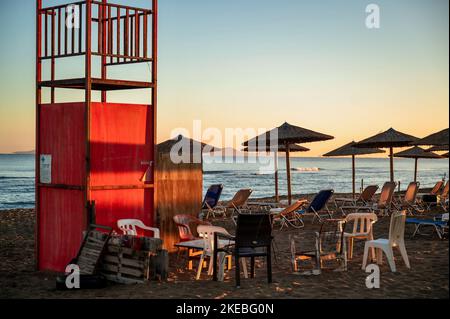 Roter Rettungsschwimmer Turm, Sonnenschirm und Stuhl am leeren Strand in idyllischer Sonnenaufgangsbeleuchtung. Amoudara, Kreta, Greec. Stockfoto