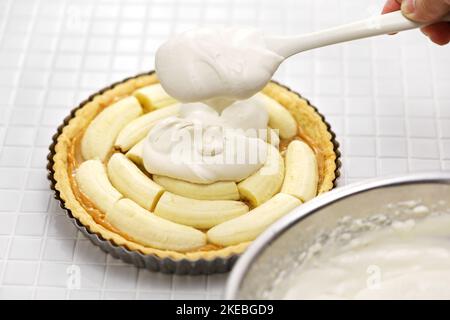 Klassisches Banoffee-Pie-Rezept; die Schlagsahne auf die Bananen geben. Stockfoto