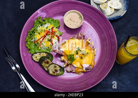 Eier Benedikt (pochierte Eier) auf gegrilltem Schinken mit holland-Sauce auf belgischen Waffeln mit gegrillten Zucchini mit Bananenplatte und einer Tasse Passionssaft Stockfoto