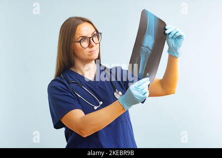 Ärztin untersucht Röntgenbild, bei dem eine Verletzung auf blauem Hintergrund diagnostiziert wird Stockfoto