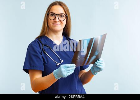 Ärztin untersucht Röntgenbild, bei dem eine Verletzung auf blauem Hintergrund diagnostiziert wird Stockfoto