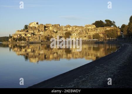 Das historische Zentrum von Anguillara Sabazia spiegelt sich im Bracciano-See wider, der vom Licht des Sonnenuntergangs erleuchtet wird Stockfoto