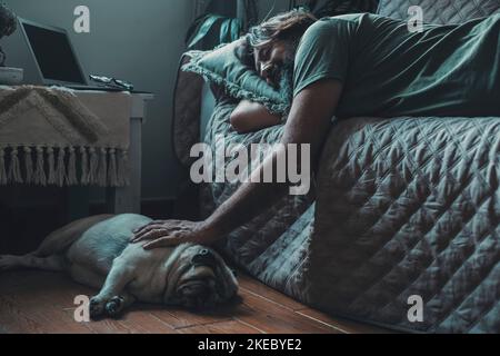 Liebe und Freundschaft mit Mensch und Hund. Tierhalter leben in Freundschaft mit Mops. Rüde schläft mit seinem Hund. Hausbesitzer und alter Welpe, die sich auf dem Sofa und dem Boden zusammenschellen, sind ein Lifestyle-Konzept für Hunde Stockfoto