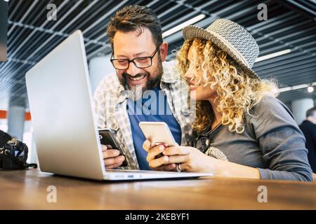 Reisen und moderne alternative Arbeitsplätze mit Laptop. Pärchen benutzte am Flughafen Telefone und Computer und wartete auf die Abreise. Mann und Frau lächeln und genießen die Online-Verbindung. Reisenden und Technologie Leben Stockfoto