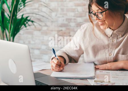 Lächelnde Frau schreiben Notizen sehen Webinar Studie Arbeit auf Laptop, junge Schüler lernen Computer Kurs hören Vorlesung Ausbildung Dolmetscher online Lehrer übersetzen Klasse Stockfoto