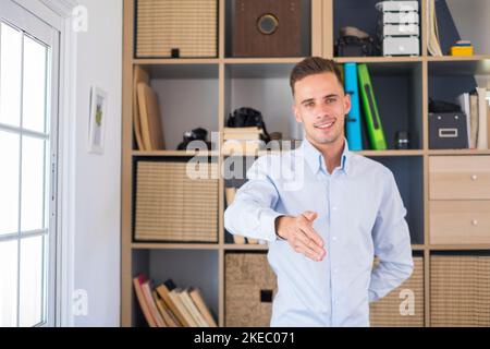 Porträt eines lächelnden, gutaussehenden Geschäftsmannes, der die Hand ausstreckte, um die Kamera zu schütteln. Freundlicher kaukasischer Mann begrüßt oder begrüßt den Kunden, indem er ihm bei einem Geschäftstreffen die Hände schüttelt Stockfoto