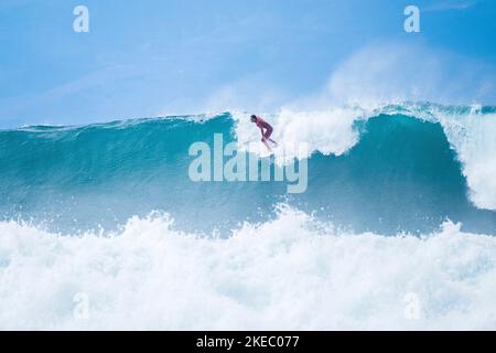 Ein Mann reitet auf einer großen und extremen blauen Welle im Ozean - im Sommer und genießt den Urlaub Stockfoto