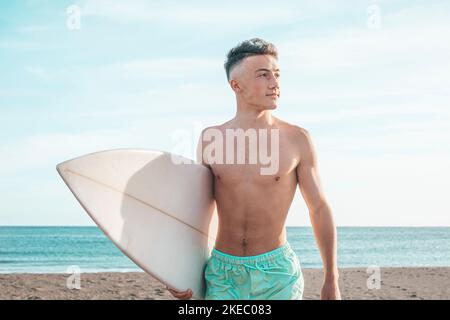 Portrait von schönen jungen Mann zu Fuß am Strand mit Sein Surfbrett bereit, Wellen zu reiten und surfen gehen in Seine Urlaubszeit Stockfoto