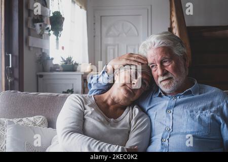 Nachdenkliche traurige ältere Mann und Frau entspannen auf dem Sofa im Wohnzimmer des modernen Hauses. Rentnerpaar tröstet sich gegenseitig von depressiven Emotionen, während sie zu Hause auf der Couch sitzen Stockfoto