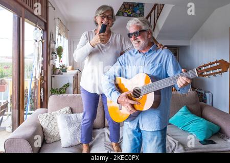 Fröhliche und lustige Paare alter und reifer Menschen, die Spaß haben und zu Hause eine gemeinsame Party machen, singen und tanzen, um die Gitarre drinnen zu spielen. Urlaub oder sogar feiern Konzept. Stockfoto