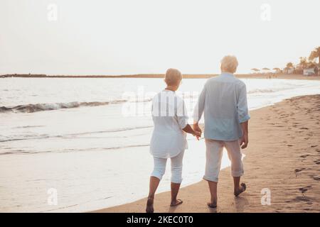 Ein paar ältere Leute, die gemeinsam auf dem Sand spazieren und sich am Strand amüsieren und den Moment genießen. Zwei niedliche Senioren in der Liebe Spaß haben. Stockfoto