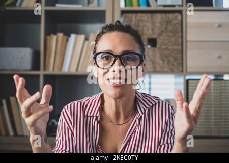 Kopfaufnahme Porträt selbstbewusste Geschäftsfrau Coach trägt Brille Blick auf Kamera und sprechen, Mentor Speaker hält Online-Lektion, erklären, sitzen am hölzernen Schreibtisch in einem modernen Schrank Stockfoto