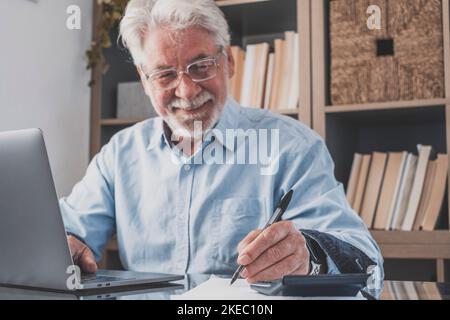 Alte Geschäftsmann oder Buchhalter Hand halten Stift Schreiben Notizen und Online-Arbeit. Leitender Mann, der am Laptop arbeitet und Konten macht, arbeitet im Heimbüro und erstellt schriftliche Aufzeichnungen Stockfoto