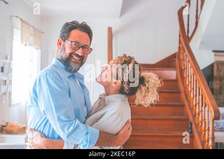 Glückliches kaukasisches Paar umarmt sich im Wohnzimmer. Liebevoller Ehemann und Ehefrau, die sich zu Hause umarmen. Liebevoller Mann und Frau verbringen gemeinsam Freizeit in einer modernen Wohnung Stockfoto