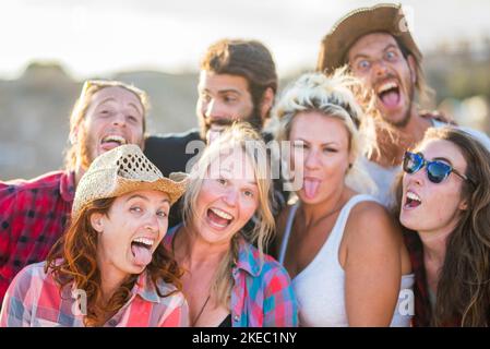 Eine Gruppe von sieben Personen, die zusammen die Kamera betrachten Verrückte und lustige Gesichter Ausdrücke - Spaß und glücklich kaukasischen Leute - Cowboy und Cowgirl in einer Ranch, die Spaß haben Genießen Stockfoto
