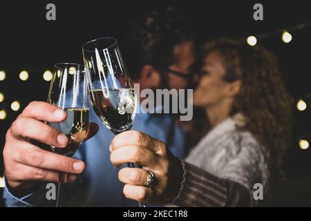 Zärtliches kaukasisches Paar küsst sich beim Toasten von Sektgläsern zur Feier der Party im neuen Jahr. Liebevoller Ehemann und Ehefrau küssen sich beim Feiern mit Weißweingläsern in den Händen Stockfoto
