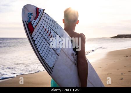 Nahaufnahme eines Mannes, der mit ihm am Strand läuft Surfbrett Surfen im Sommer mit dem Sonnenuntergang Stockfoto