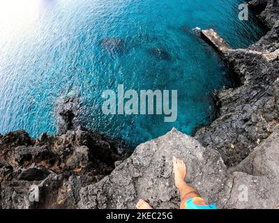 Ein Mann in Pov oder eine erste Person, die von einer Klippe zum Wasser des Meeres oder des Ozeans am Strand springen Stockfoto