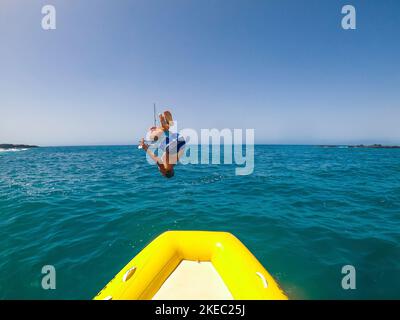 Teenager und junger Mann springen und machen einen Backflip in Das Boot oder Schlauchboot zum Wasser Spaß und Genießen Sie Sommerferien im Meer - kaukasische Menschen an Der Strand mieten ein Boot Stockfoto