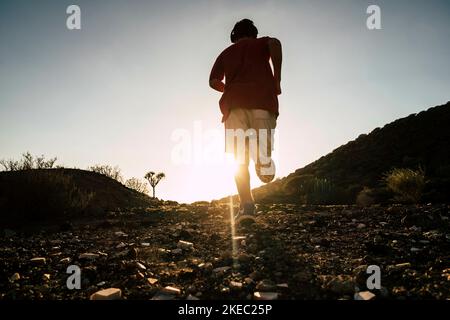 Ein Teenager läuft und joggt allein in den Bergen beim Sonnenuntergang auf den Felsen - gesundes und Fitness-Lifestyle-Konzept - Himmel im Hintergrund Stockfoto