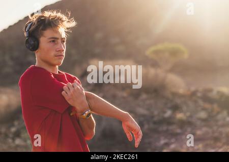 Ein Teenager läuft oder joggt allein in den Hügeln - Mann Stretching Musik hören mit Kopfhörern nach einem Übungssitzung Stockfoto