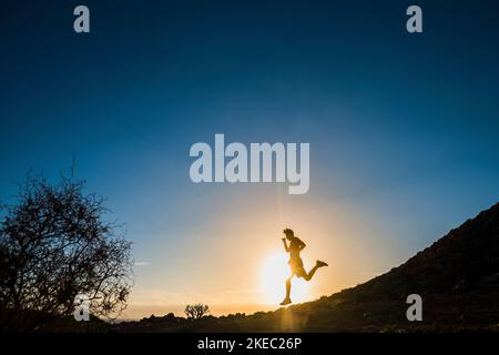 Ein Teenager läuft und joggt allein in den Bergen beim Sonnenuntergang auf den Felsen - gesundes und Fitness-Lifestyle-Konzept - man Workout Stockfoto