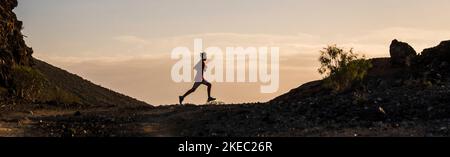 Ein junger Mann, der allein in den Bergen und am Boden läuft, um gesund und aktiv zu sein - ein Teenager, der Sport macht und Trekking-Lifestyle betreibt Stockfoto