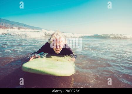 Ein Senior versucht, allein im Wasser des zu surfen Strand und Surfen lernen - reifer alter Mann wartet auf Die Wellen mit seinem langen Surfbrett Stockfoto