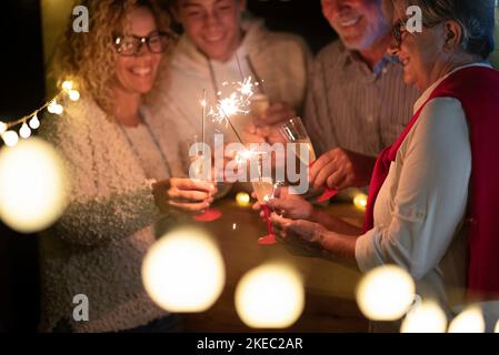 Gruppe von vier Personen feiert die 2021 zusammen mit Wunderkerzen Und Wein - Spaß haben in einer fröhlichen Party Stockfoto