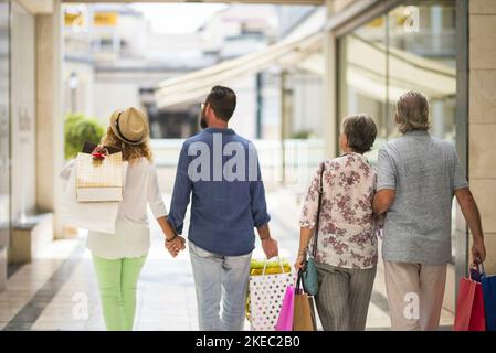 Gruppe oder Familie, die zusammen in einem Einkaufszentrum einkaufen gehen Und halten Einkaufstaschen - Erwachsene und Senioren schauen Die Geschäfte oder Geschäfte Stockfoto