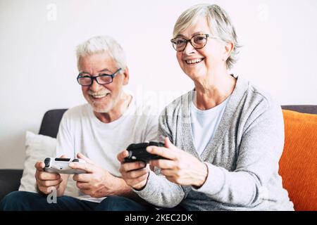 Ein paar Senioren und ältere Menschen, die auf dem Sofa und dem fernseher schauen und Videospiele zu Hause mit Steuergeräten spielen - ein Lebensstil in Innenräumen Stockfoto