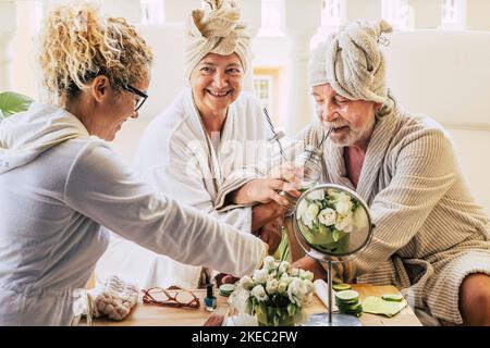 Ein paar von zwei Senioren genießen ein Spa und Massage Verrat Zusammen mit einer Hilfe helfen ihnen - trinken Cocktails und Spaß am Lächeln Stockfoto