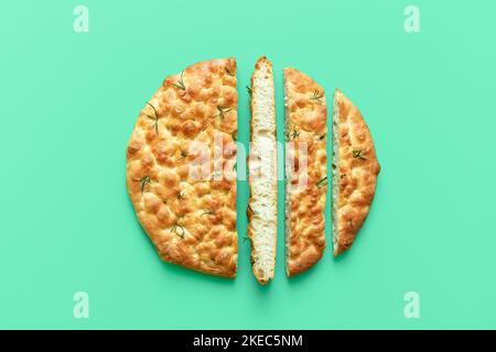 Oben mit hausgemachter Focaccia auf einem grünen Tisch. Italienisches Fladenbrot in Scheiben, im Ofen gebacken, minimalistisch auf einem farbenfrohen Hintergrund. Stockfoto