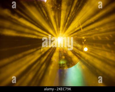 Diskokugel, die goldenes Licht an einer Party-Location reflektiert. Helle Lichtstrahlen der kleinen Spiegelstücke, die den Raum erhellen. Nebel macht Licht sichtbar. Stockfoto