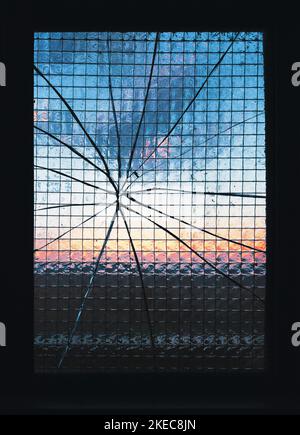 Sonnenuntergang durch rissene Glasscheiben eines vandalensicheren, verstärkten Industriefensters Stockfoto
