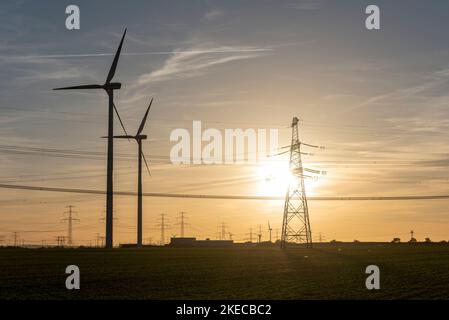 Zwei Windturbinen stehen neben einem Strommast. Stockfoto