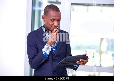 Junger Geschäftsmann, der im Büro steht und beim Arbeiten an einem digitalen Tablet nachdenkt. Stockfoto