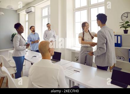 Mann und Frau grüßen sich gegenseitig und schüttelten die Hände und ihre Kollegen schauten sie im Büro an. Stockfoto