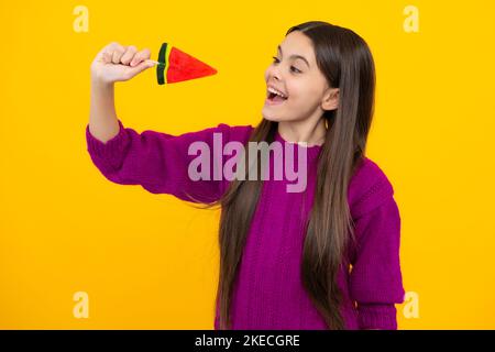 Lustiges Kind mit Lutscher auf gelbem isoliertem Hintergrund. Süßes Kindheitsleben. Teen Mädchen mit yummy Karamell Lollipop, Süßwarenladen. Teenager mit Stockfoto