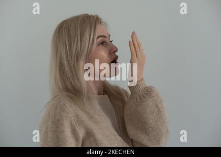 Junge Frau überprüft ihren Atem mit der Handfläche. Stockfoto