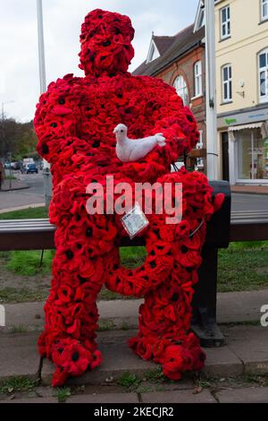 Chesham, Buckinghamshire. VEREINIGTES KÖNIGREICH. 11. November 2022. Eine auffällige Figur zum Gedenktag, in der ein Mann mit roten Mohnblumen auf einem Sitz in Chensham neben dem Kriegsdenkmal sitzt und eine weiße Taube in der Hand hält. Quelle: Maureen McLean/Alamy Live News Stockfoto